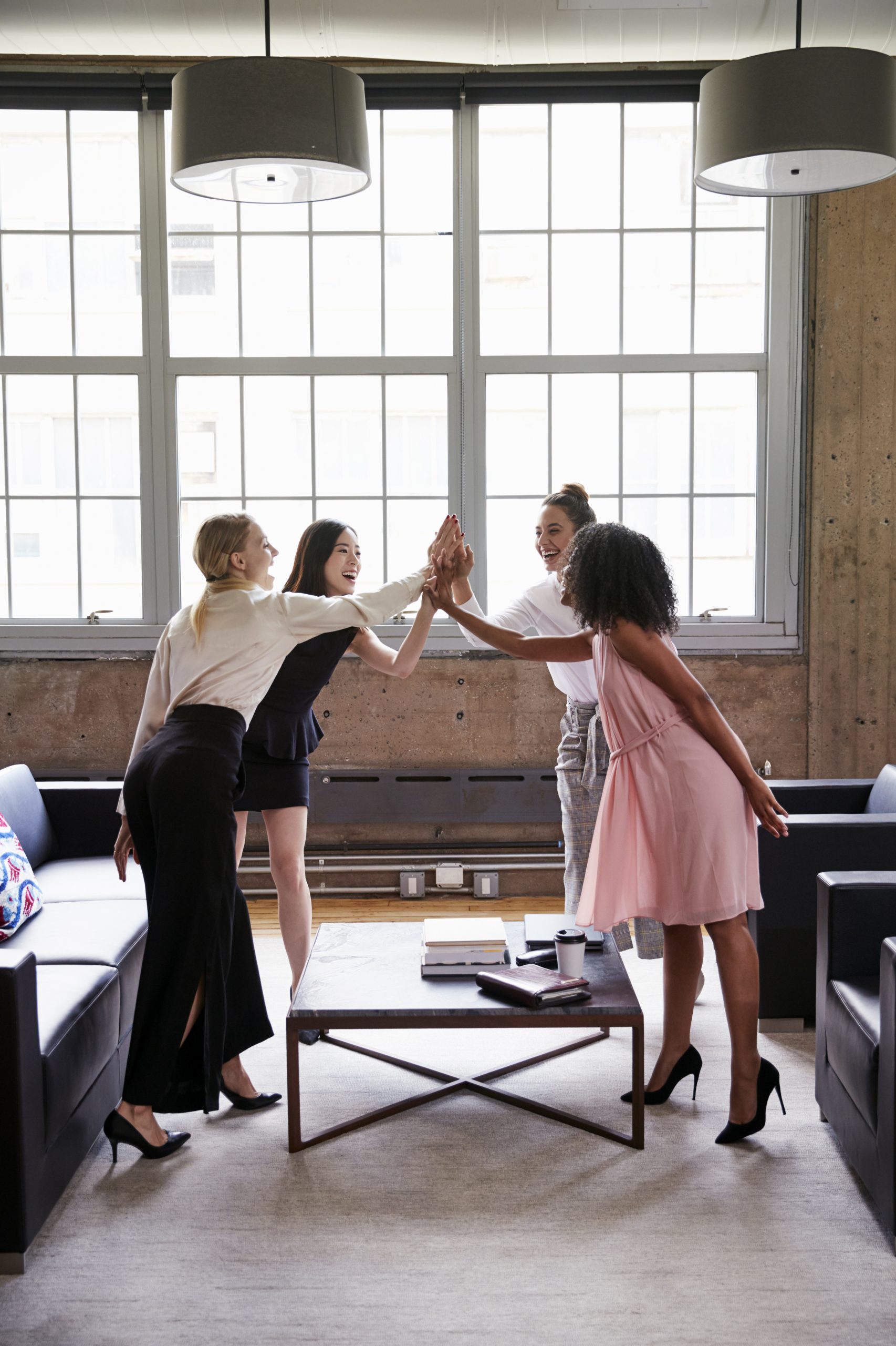 Female colleagues high five at a casual meeting, vertical